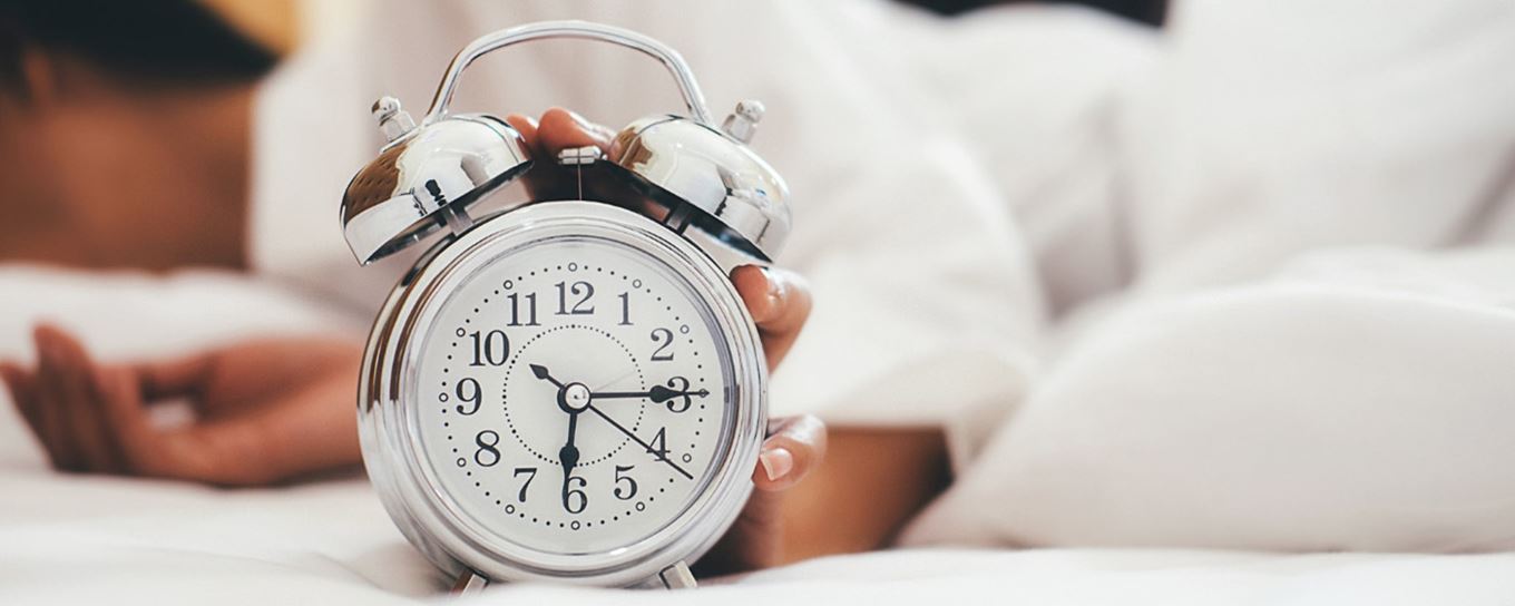 Vrouw ligt in bed en drukt wekker uit