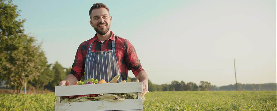 Vrolijk kijkende boer met gestreepte schort voor en een krat in zijn handen | Dit is de tijd van doen | a.s.r.