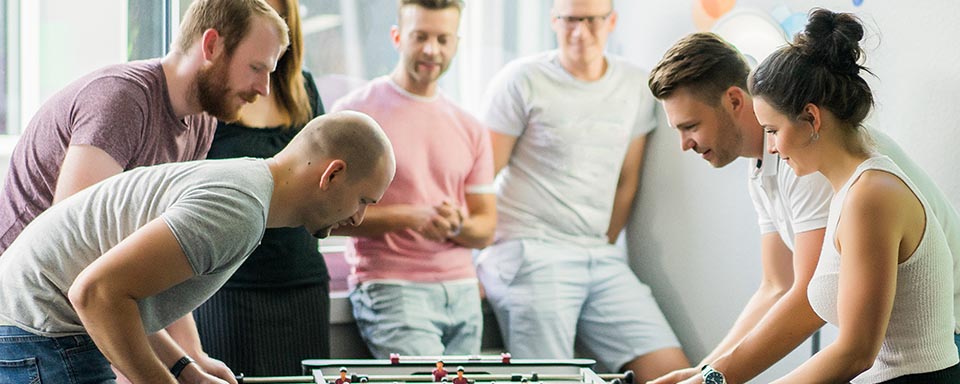 Jongelui spelen een potje tafelvoetbal en anderen kijken toe | a.s.r.