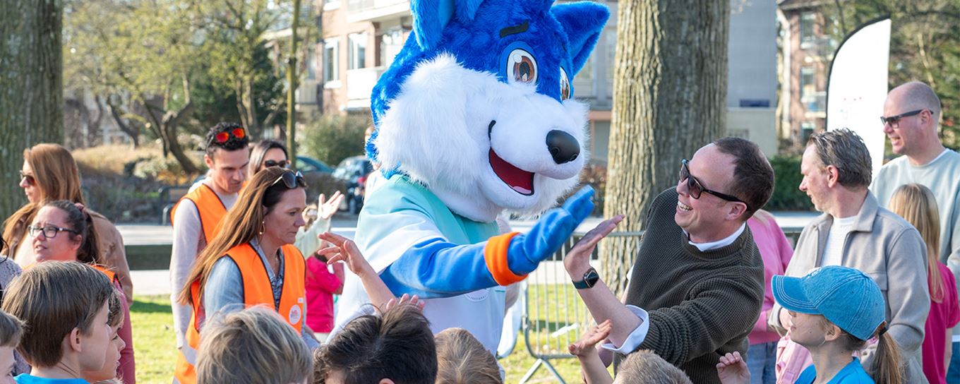 een man doet lachend een high five met fiero de mascotte. eromheen zijn allemaal kinderen en ouders