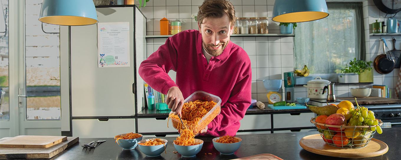 man schept spaghetti vanuit een grote bak in vier schaaltjes