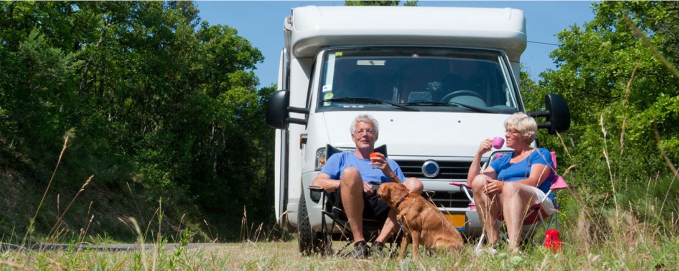 man vrouw en hond zitten met een kop koffie voor hun kamper