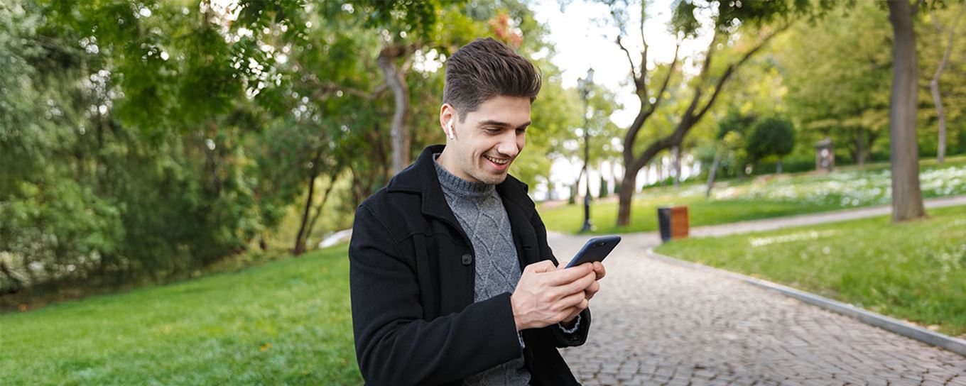 Jonge man staand in een park met zijn mobiele telefoon in zijn handen