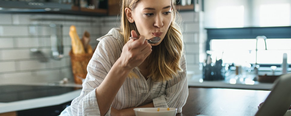 Vrouw achter laptop in keuken vraagt zich iets af